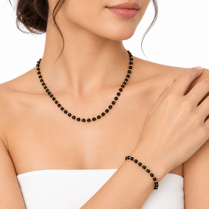 Modelka na białym tle w zestawie biżuterii boho z czarnych koralików, naszyjnik i bransoletka